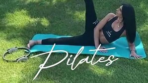 A person performing a Pilates exercise on a mat in a grassy outdoor area with palm trees and a hill in the background. - Female Resort (San Felice Circeo)