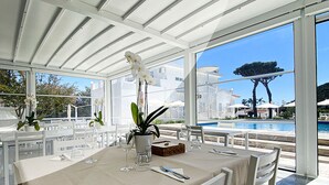 An outdoor dining area with white tables and chairs, a pool in the background, and a clear view of the surrounding landscape. - Female Resort (San Felice Circeo)