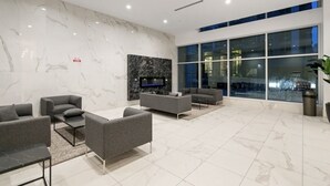 Een moderne lobby met marmeren wanden, een open haard, grijze banken en grote ramen.