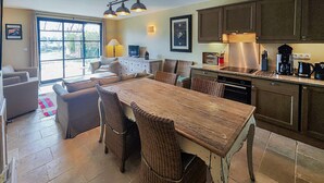 Eine moderne Küche mit Essbereich, ausgestattet mit einem großen Holztisch, Korbstühlen und Edelstahlgeräten.