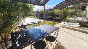 Eine Terrasse im Freien mit Tisch und Stühlen, umgeben von Grünpflanzen und einem Pergola-Überbau.