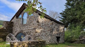 A rustic stone building with a sloped roof, a large arched window, and a small door.