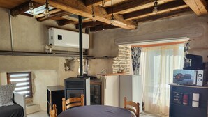 A rustic kitchen with a wood stove, a dining table with chairs, a refrigerator, and a window with curtains.