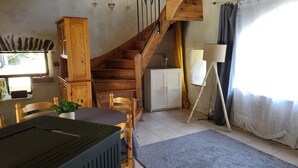 A rustic room with a wooden staircase, a dining table with chairs, a cabinet, and a lamp.