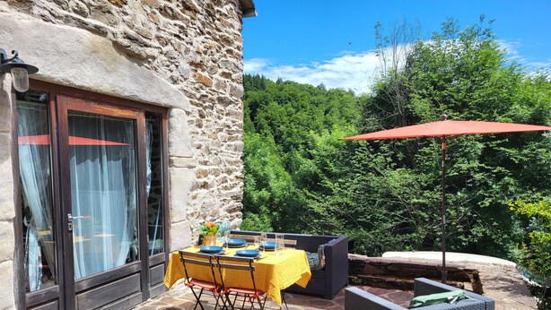 A stone building with a dining area featuring a table set with blue plates and a yellow tablecloth, outdoor seating, and a red umbrella.