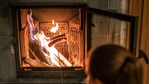 A person sitting by a fireplace with logs burning.