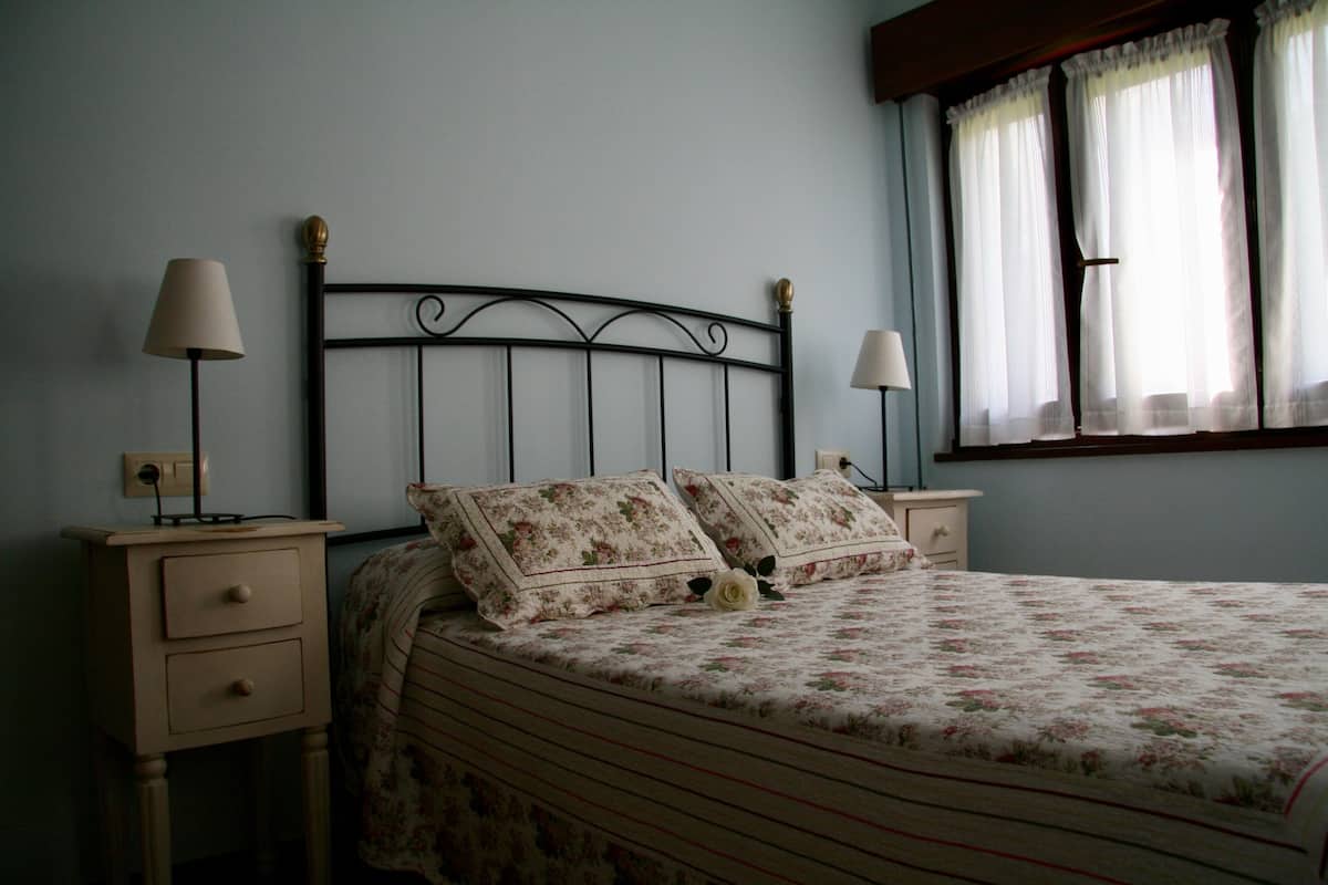 A bedroom with a bed, two nightstands, and a window with curtains.
