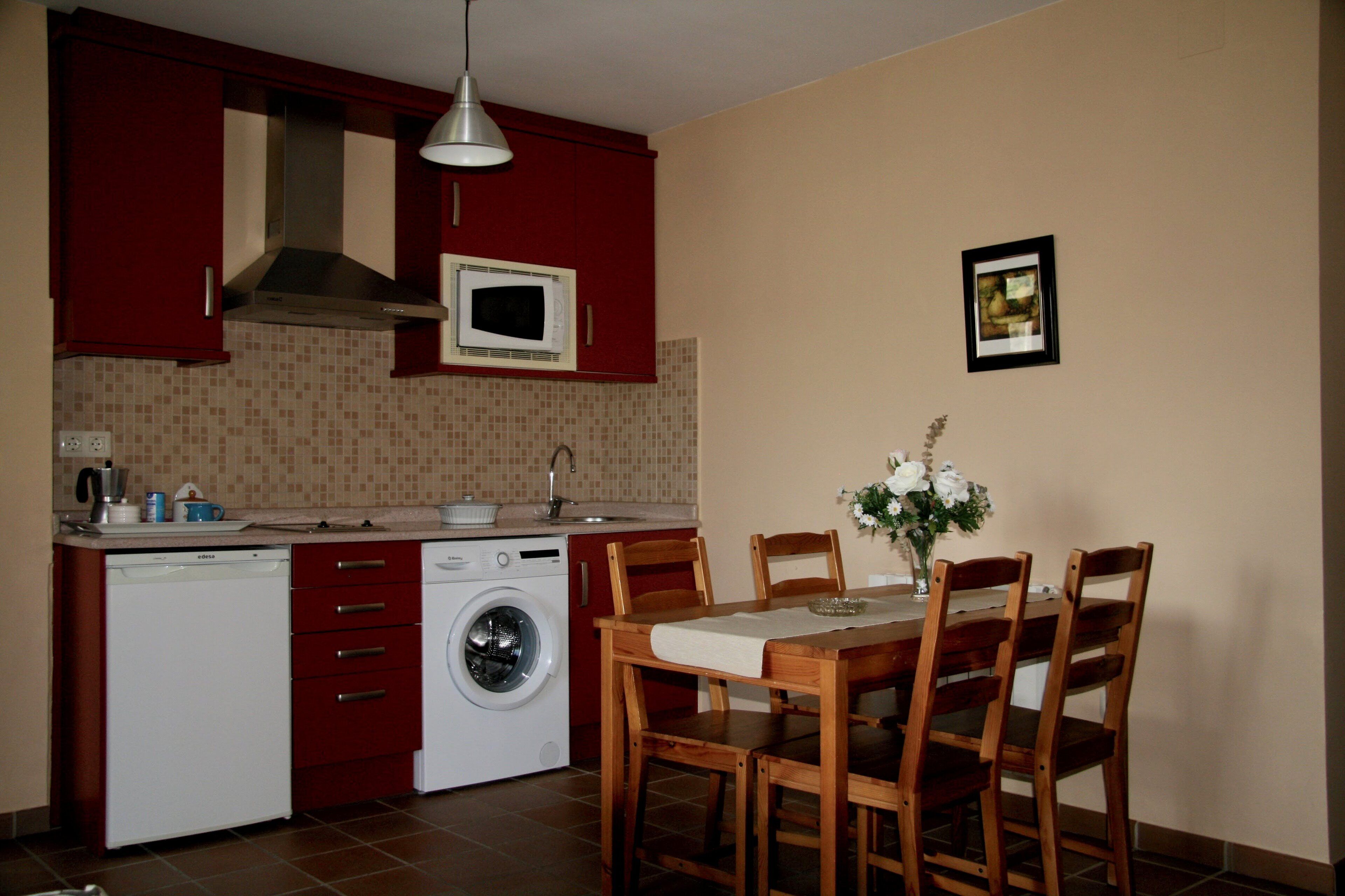 Cocina compacta equipada con lavavajillas, microondas y lavadora. Cuenta con una mesa de comedor con sillas y un florero con flores.