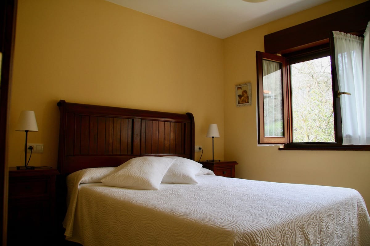 A neatly made bed with a wooden headboard, two bedside lamps, and a window with curtains.
