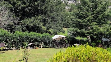 Un jardín con un conjunto de columpios de madera, un cobertizo pequeño y una zona cubierta de césped.