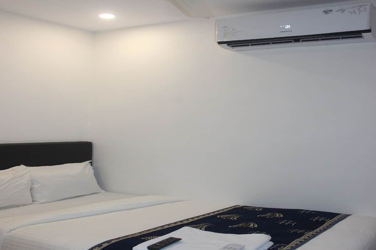 Une chambre d’hôtel avec un lit, une télécommande et un climatiseur fixé au mur.