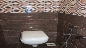 A bathroom with a white toilet, a shower, and patterned tiles on the walls. - Tanvi Guest House (Mumbai)