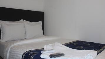 A neatly made bed with white linens, a dark blue blanket with a geometric pattern, and a remote control on the bed.