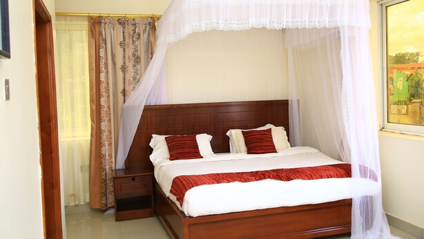 A neatly made bed with a canopy, a wooden headboard, and a nightstand with a drawer. - GLORY SUMMIT HOTEL  (Hoima)