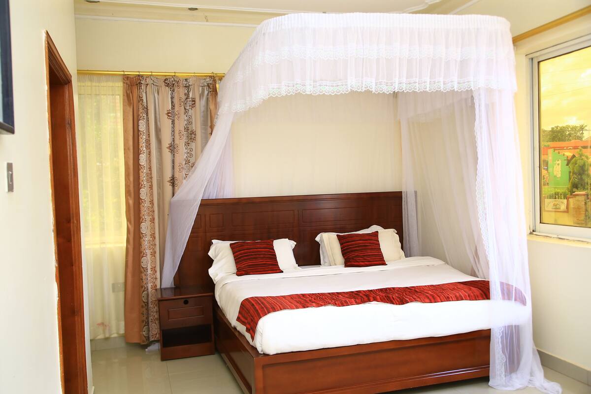 A neatly made bed with a canopy, a wooden headboard, and a nightstand with a drawer.