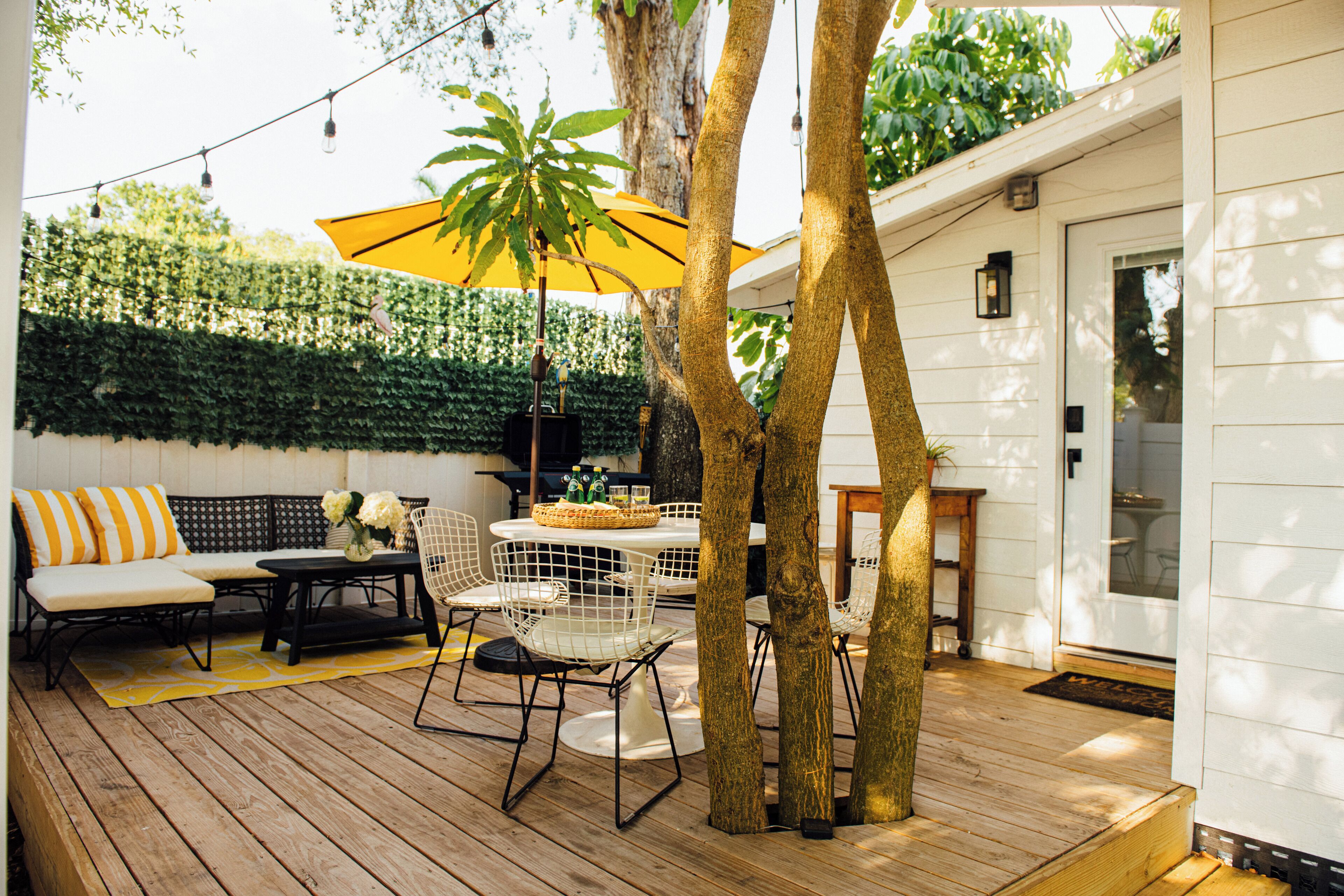 Eine Terrasse im Freien mit Holzdeck, weißer Möbel und einem gelben Sonnenschirm.