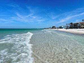 Une plage aux eaux cristallines, un rivage sablonneux et des bâtiments visibles au loin.