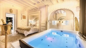 A luxurious bedroom with a large bathtub, a bed with a fluffy blanket, and a decorative mirror. - Buddha Beach Thoiry  (Thoiry)