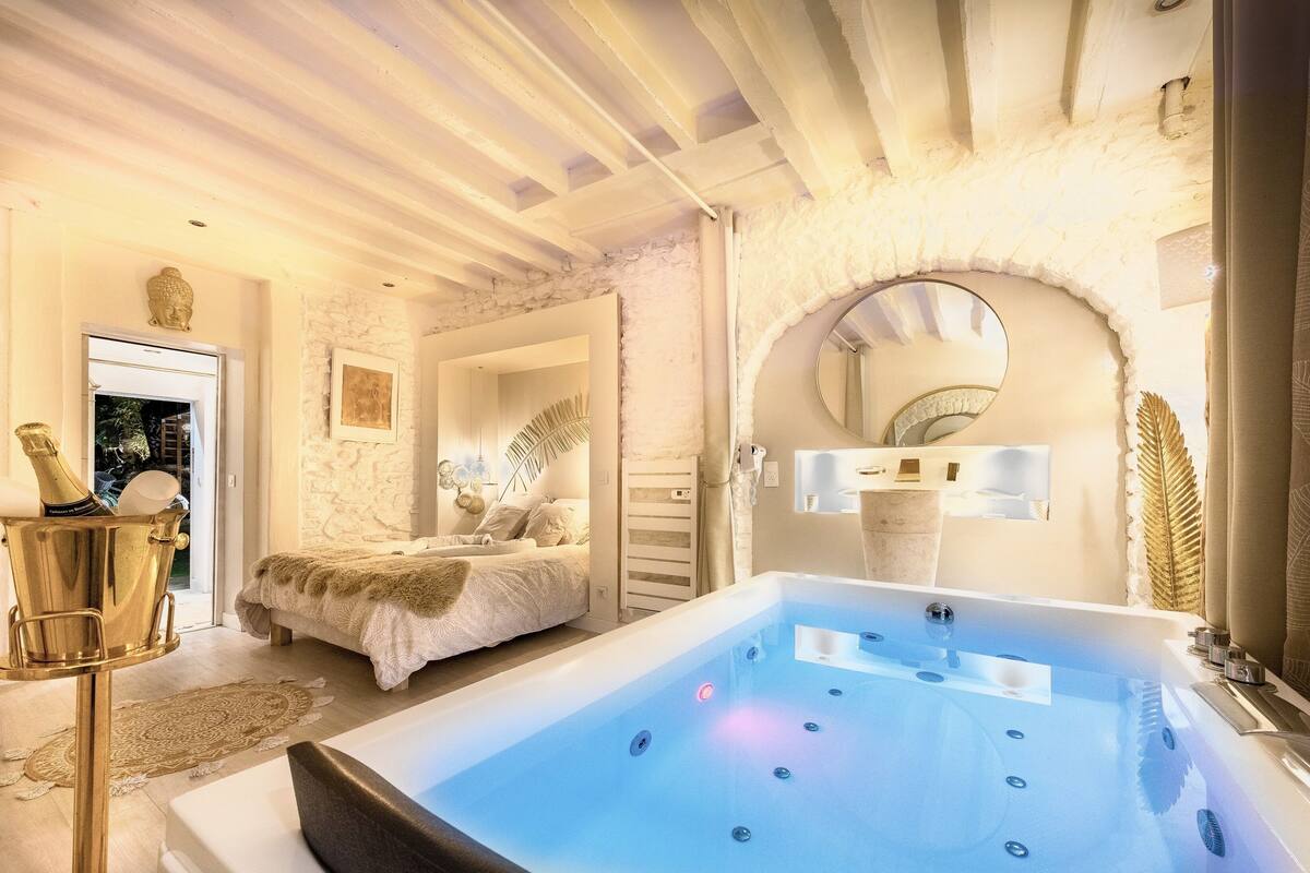 A luxurious bedroom with a large bathtub, a bed with a fluffy blanket, and a decorative mirror.