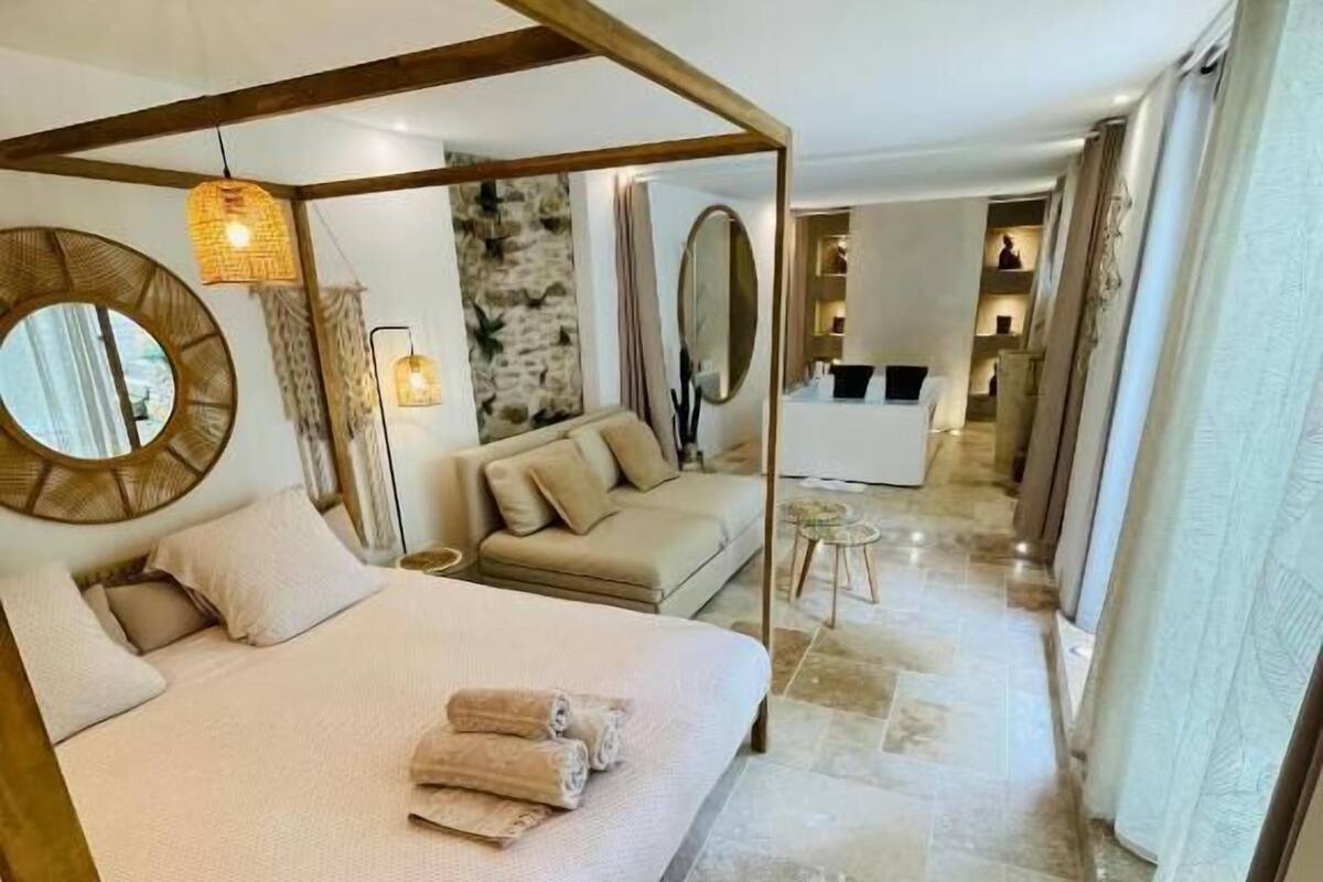 A bedroom with a four-poster bed, a round mirror, and a stone wall.