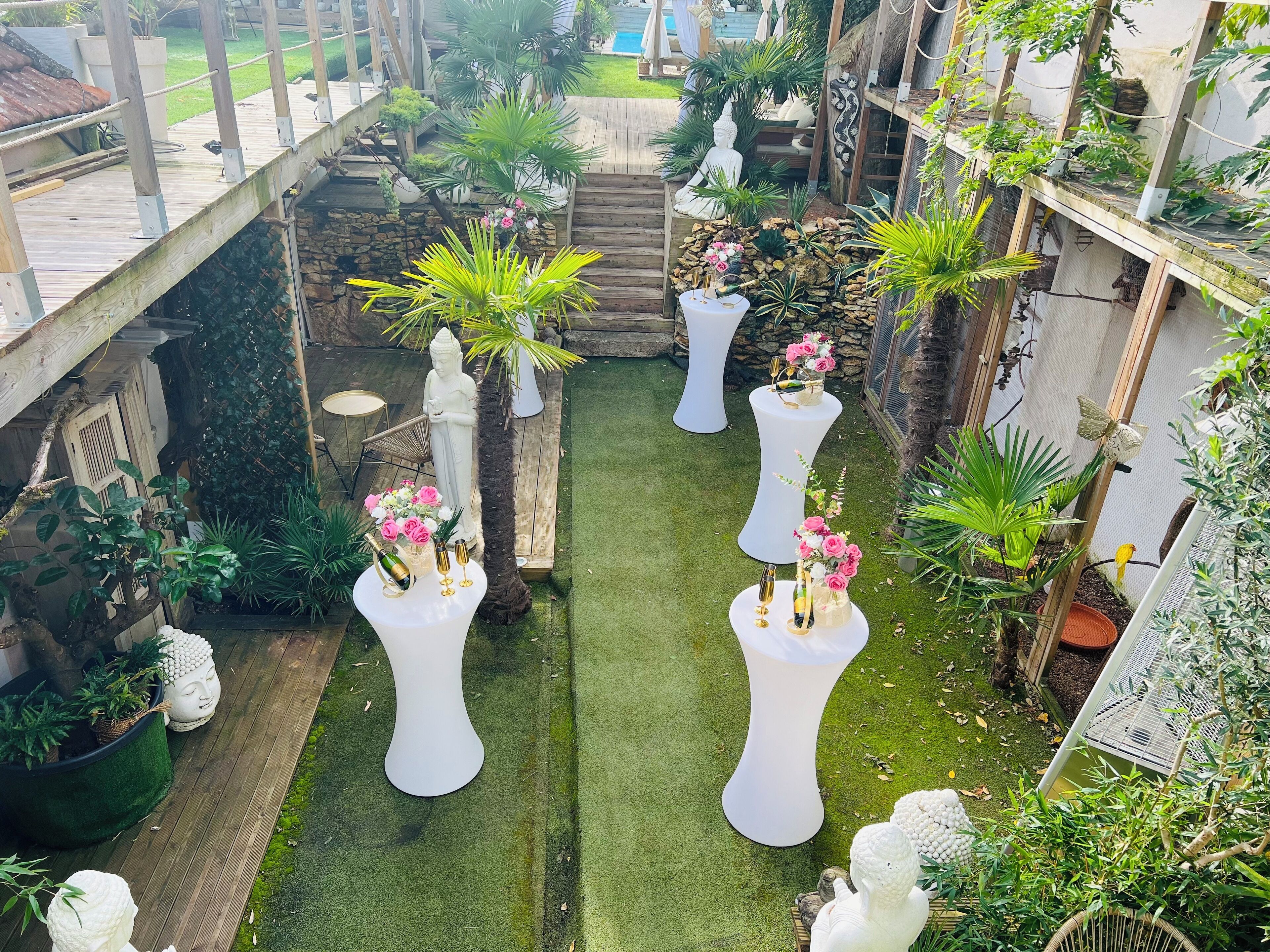 Un jardín con estatuas blancas, una terraza de madera y diversas plantas.
