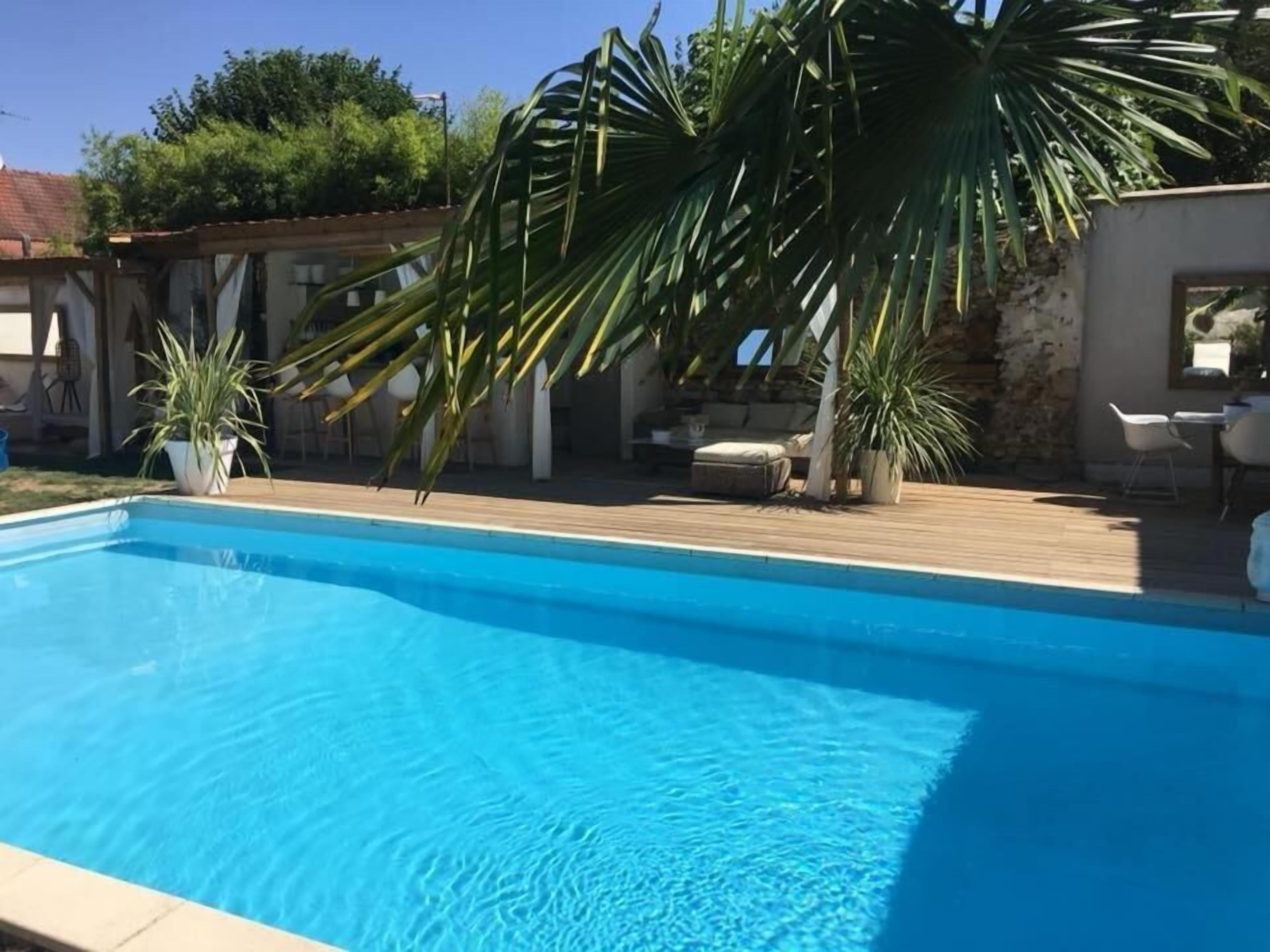 Ein Schwimmbecken mit Holzterrasse, umgeben von Kübelpflanzen und Gartenmöbeln.