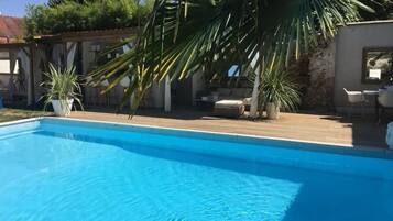 Ein Schwimmbecken mit Holzterrasse, umgeben von Kübelpflanzen und Gartenmöbeln.