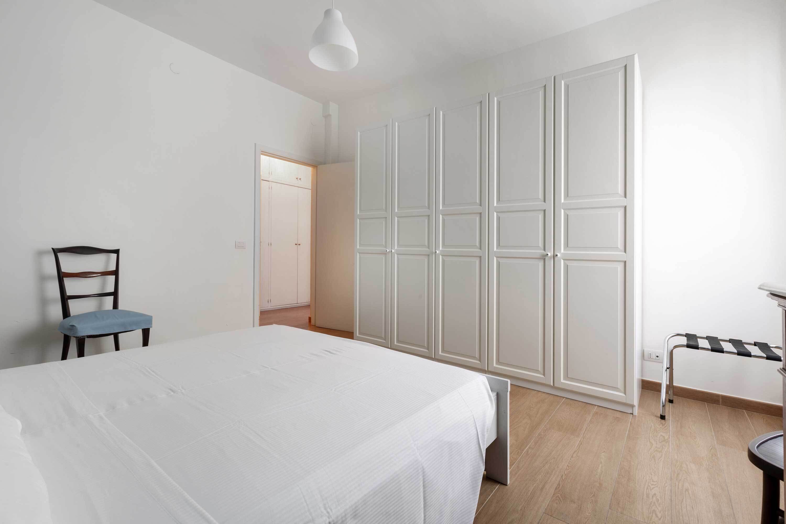 A bedroom with a bed, a chair, a wardrobe, and a small table.