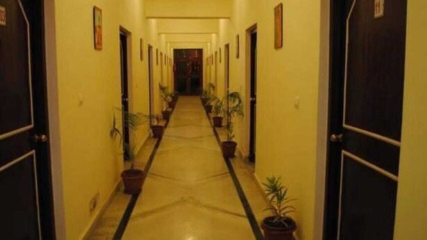 A hotel corridor with doors on both sides, potted plants along the walls, and a tiled floor. - Hotel Ambika Palace by Shiwani Associate (Agra)