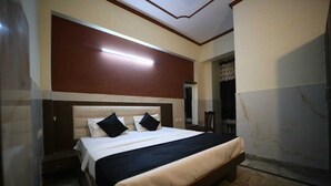A bedroom with a bed, a nightstand, a mirror, and a door. - Hotel Ambika Palace by Shiwani Associate (Agra)