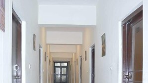 A long, narrow hallway with doors on both sides, leading to a bright room at the end. - Hotel Ambika Palace by Shiwani Associate (Agra)
