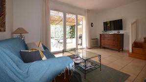 Ein Wohnzimmer mit einer Couch, einem Couchtisch, einem Fernseher, einer Kommode und einer Glastür zum Außenbereich.
