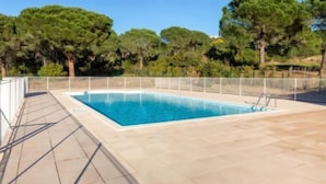 Ein Schwimmbecken im Freien mit einer gefliesten Terrasse, umgeben von einem Zaun und Bäumen.