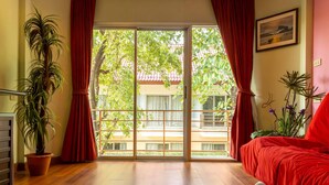 A room with a large sliding glass door leading to a balcony, a potted plant, a bed with red bedding, and a framed picture on the wall. - Kiatthada Resort (Bangkok)