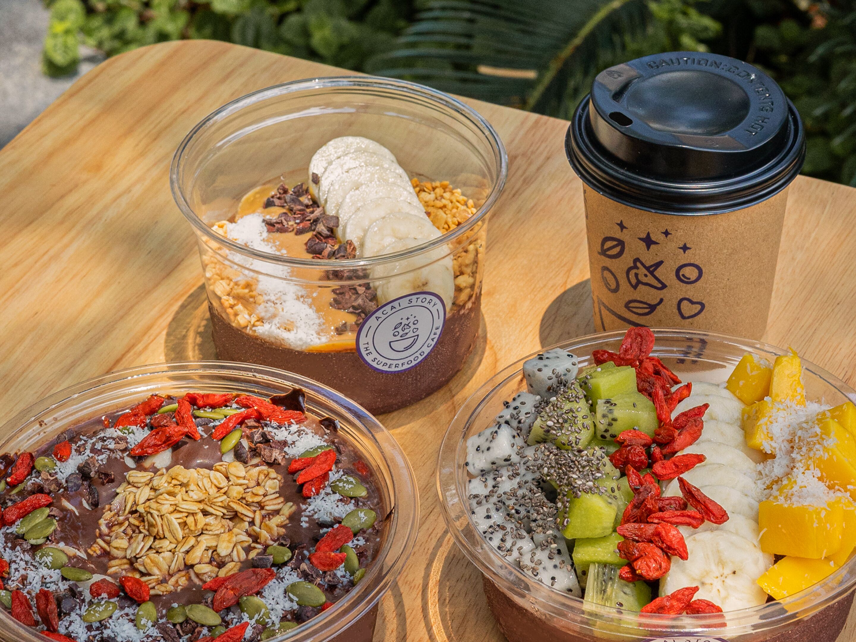 Three bowls of food and a coffee cup on a wooden table.