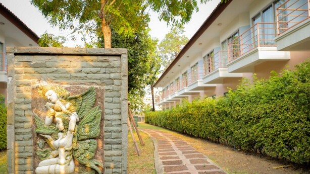 A pathway leading to a building with a stone wall featuring a relief sculpture. - Kiatthada Resort (Bangkok)