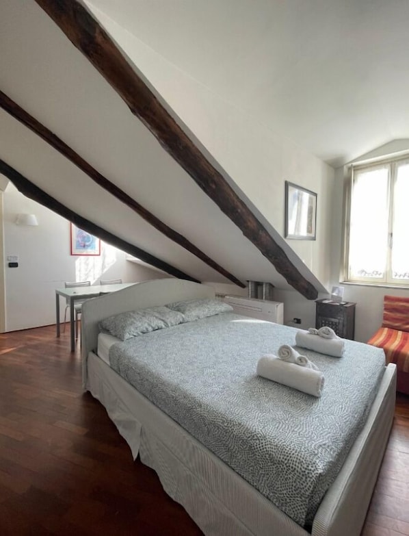Una camera da letto con soffitto spiovente, un letto con copriletto decorato, un comodino e una finestra.