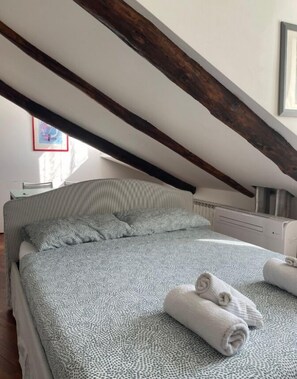 A bedroom with a sloped ceiling, a bed with a patterned bedspread, and rolled towels on the bed.
