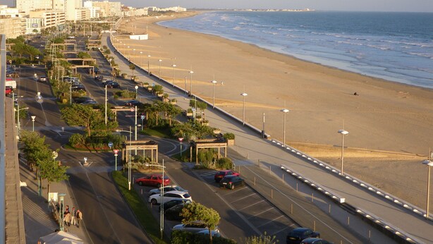 A coastal road with a beach on one side and buildings on the other.