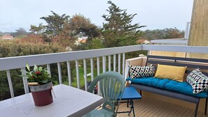 A balcony with a table, chairs, a sofa with cushions, and a potted plant.