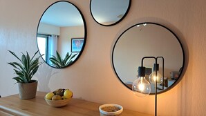 A wall with three round mirrors and a table with a potted plant, a bowl of fruit, and a lamp.