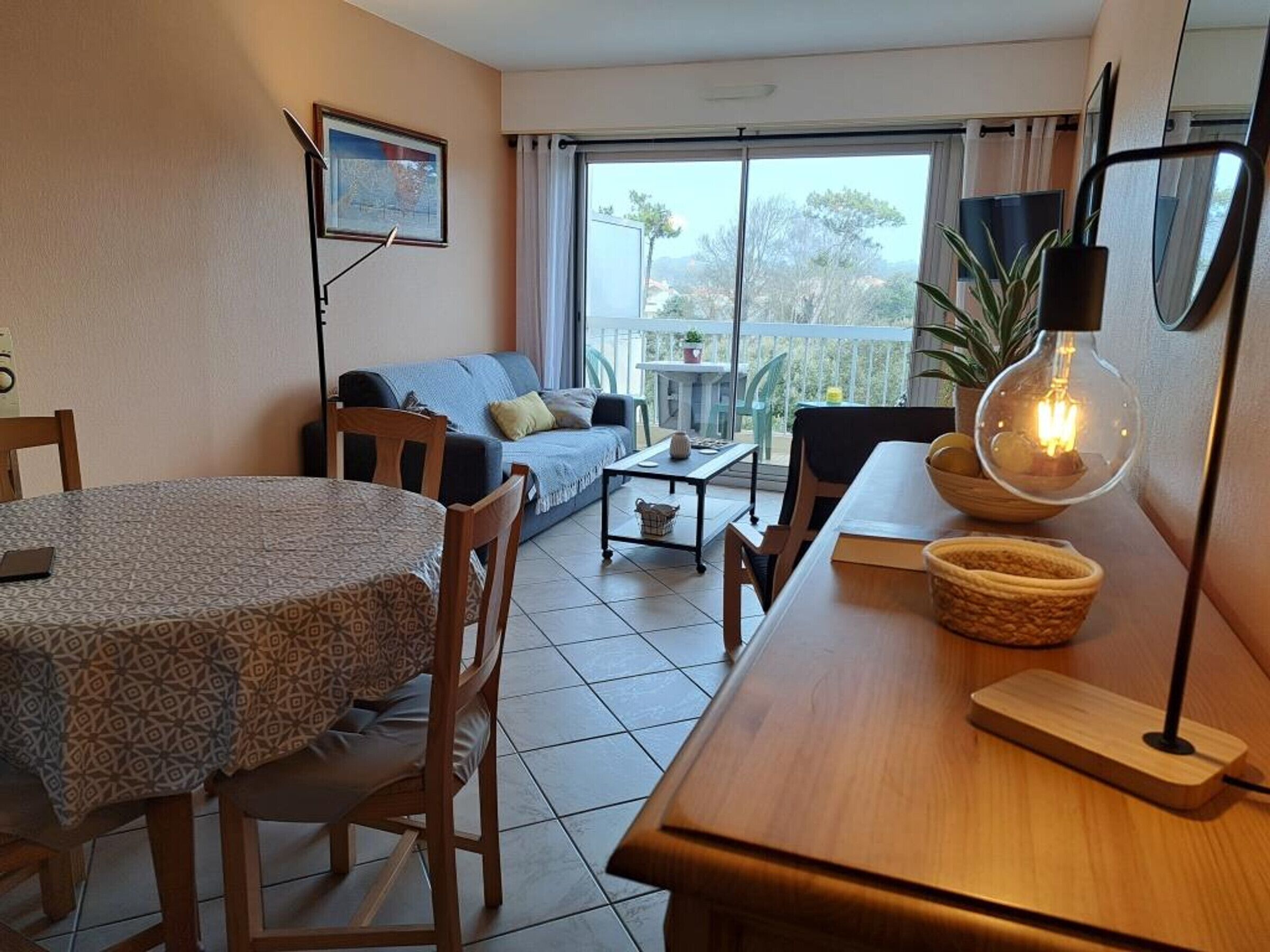 A cozy living room with a dining area, a sofa, a table, and a balcony with a view.
