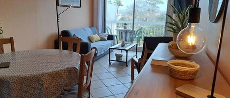 A cozy living room with a dining area, a sofa, a table, and a balcony with a view.