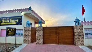 A resort entrance with a wooden gate, stone pillars, and a signboard advertising services. - The Kukas Resort (Amer)