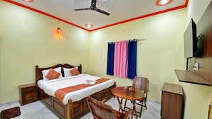 A hotel room with a bed, a desk, a chair, a ceiling fan, and a TV mounted on the wall. - The Kukas Resort (Amer)