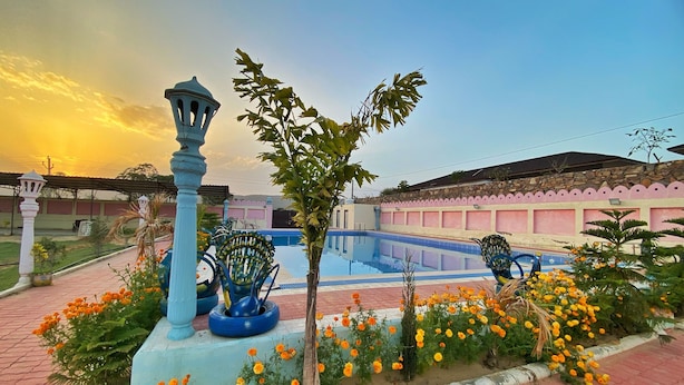 A swimming pool with a blue and white tiled deck, surrounded by a garden with marigold flowers and a decorative fountain. - The Kukas Resort (Amer)
