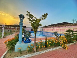 A swimming pool with a blue and white tiled deck, surrounded by a garden with marigold flowers and a decorative fountain. - The Kukas Resort (Amer)