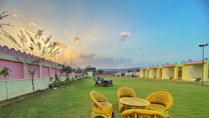 A courtyard with yellow wicker furniture, a grassy lawn, and buildings with pink and yellow walls. - The Kukas Resort (Amer)