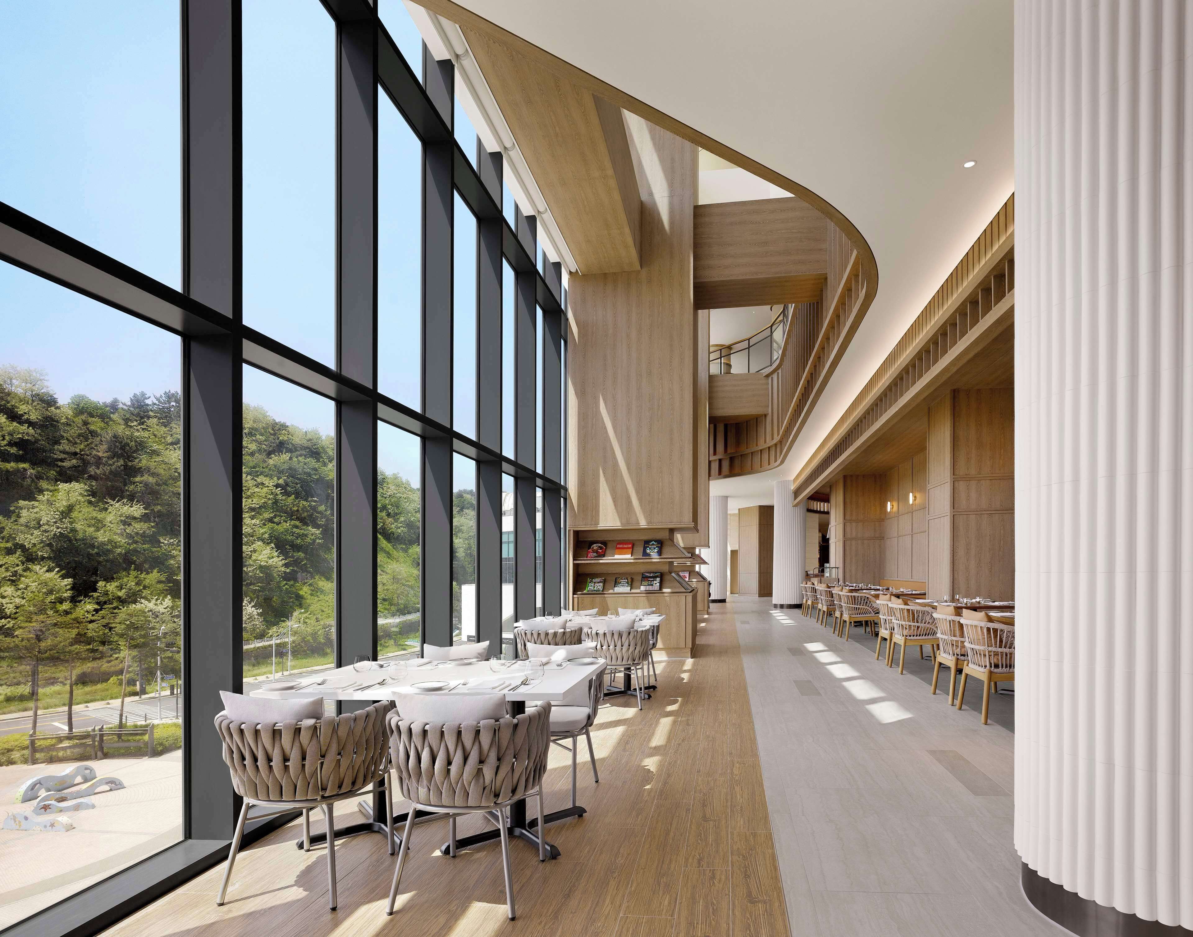 A modern dining area with large windows, a curved ceiling, and a view of greenery outside.