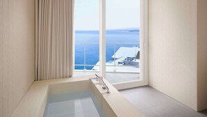 Un baño moderno con una bañera grande, una puerta corredera de vidrio que da a un balcón con vista al mar.